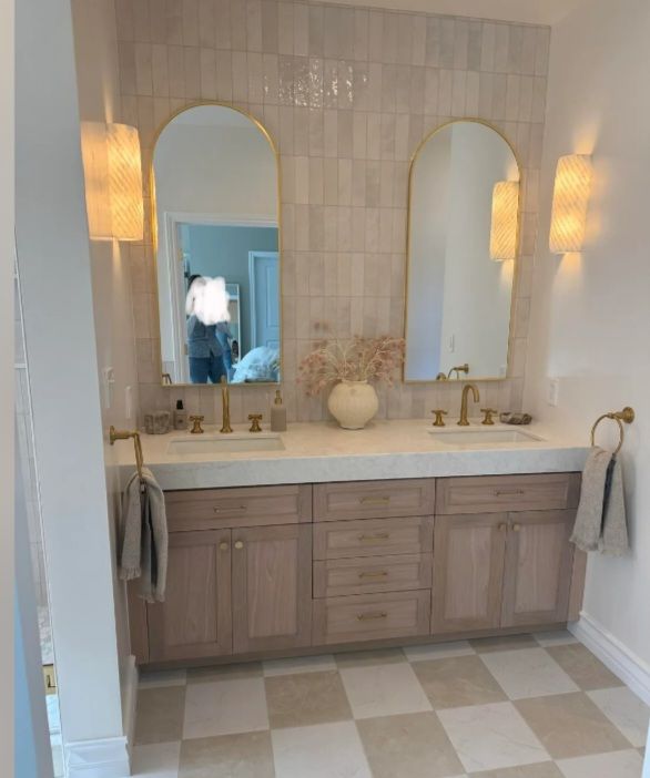 Bathroom after: wood double vanity, stone top, tiled wall, arched brass mirrors and a checkerboard floor.