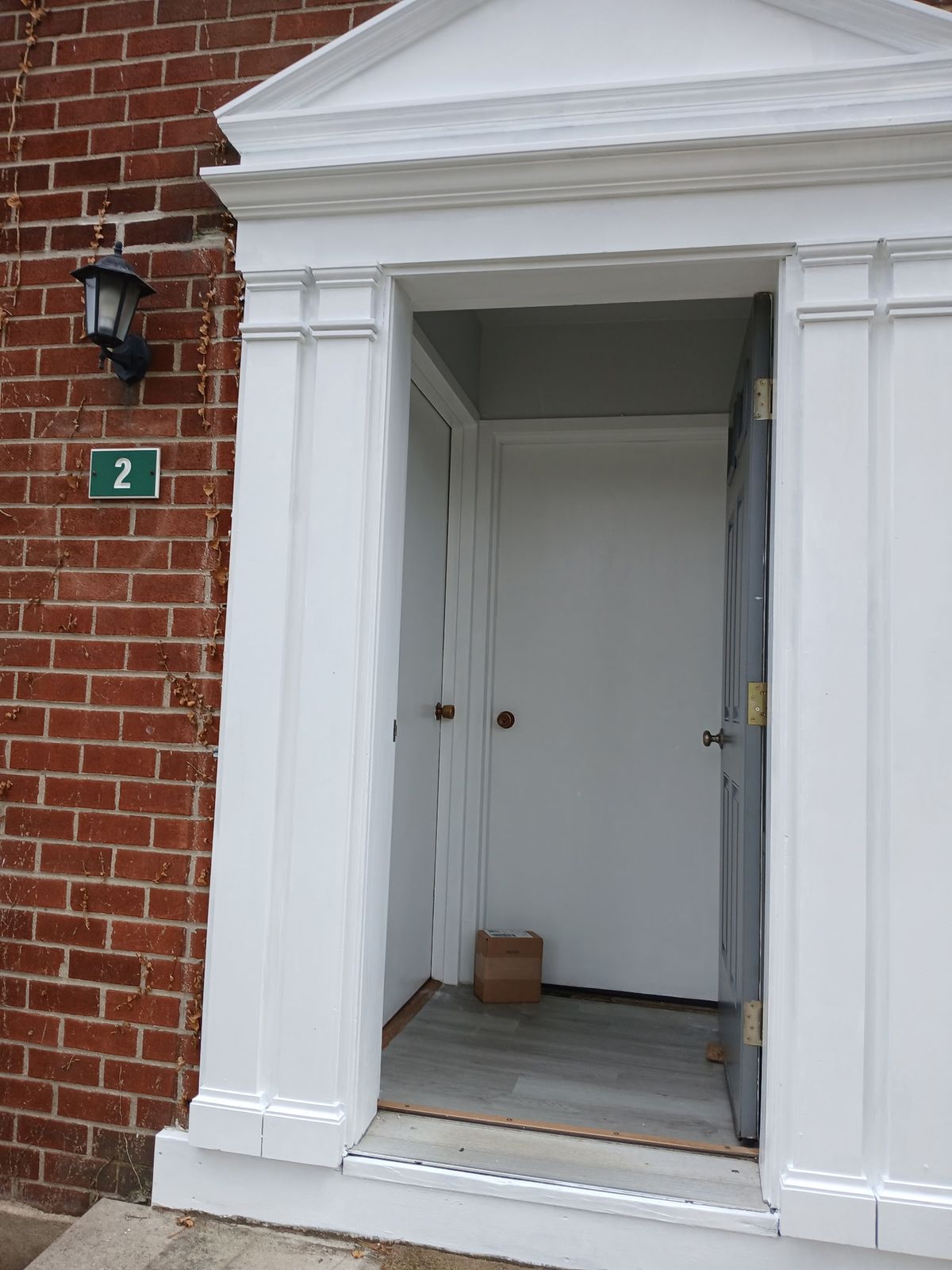 Entry 2 after: pediment, pilasters and trim freshly painted white, door open to a vestibule with a new plank floor.