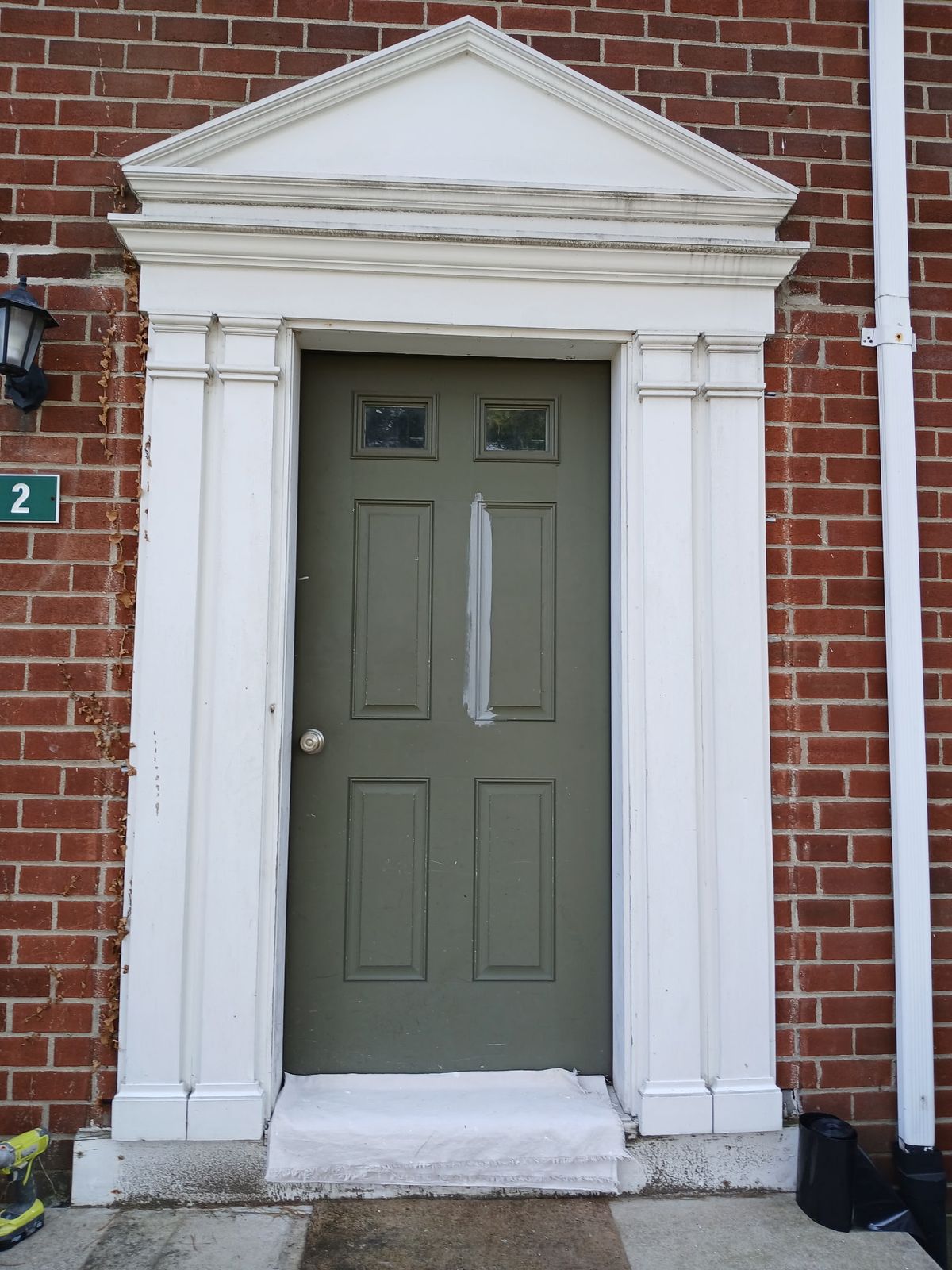 Entry 2 before: worn white pediment and pilasters around a green door, with a test patch of paint.