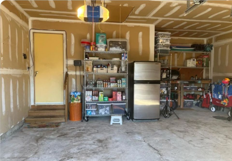 Two-car garage after: open floor with a wire shelving unit, a fridge and wall shelves.