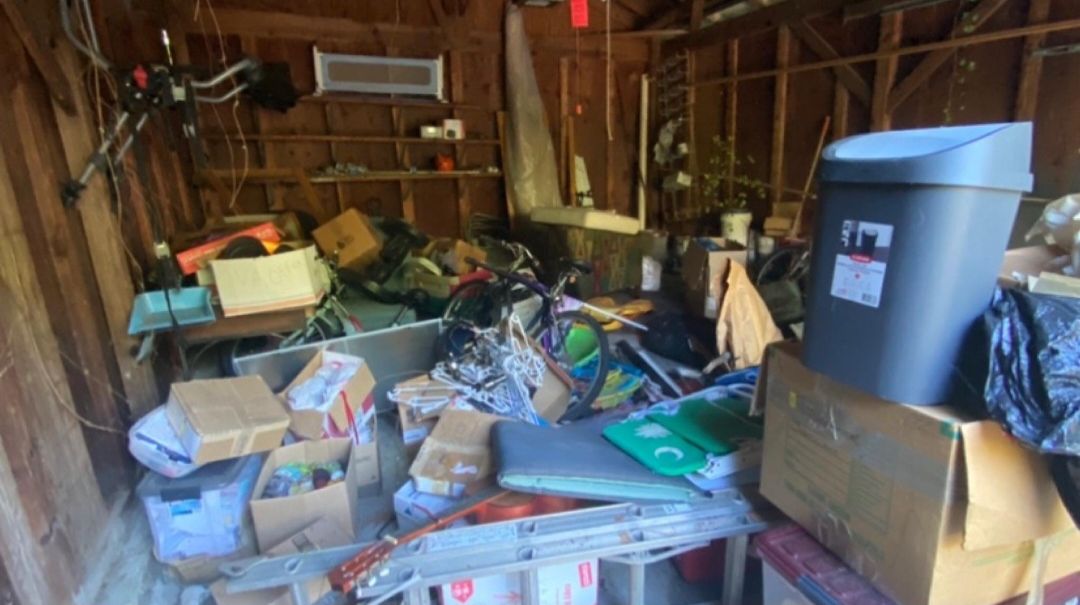 Detached garage before: boxes, bikes, bins and debris piled to waist height.