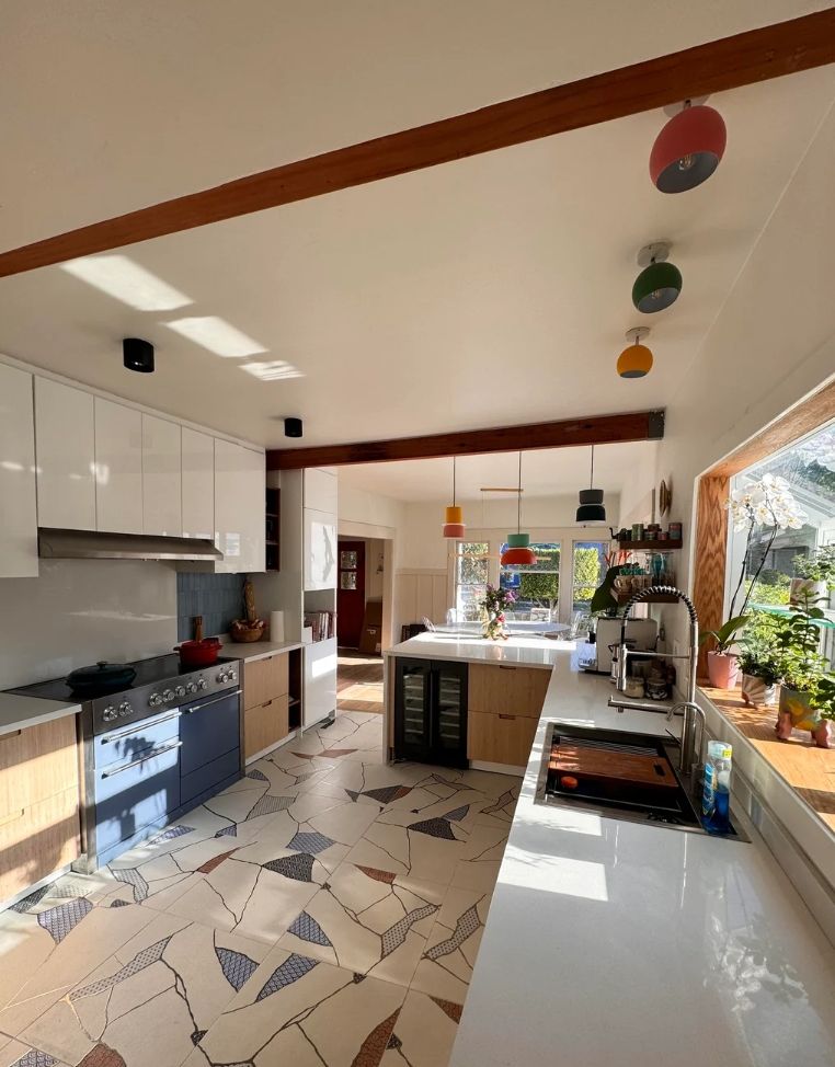 Finished open kitchen: white upper cabinets, wood lowers, a range, a long white counter and a patterned tile floor.