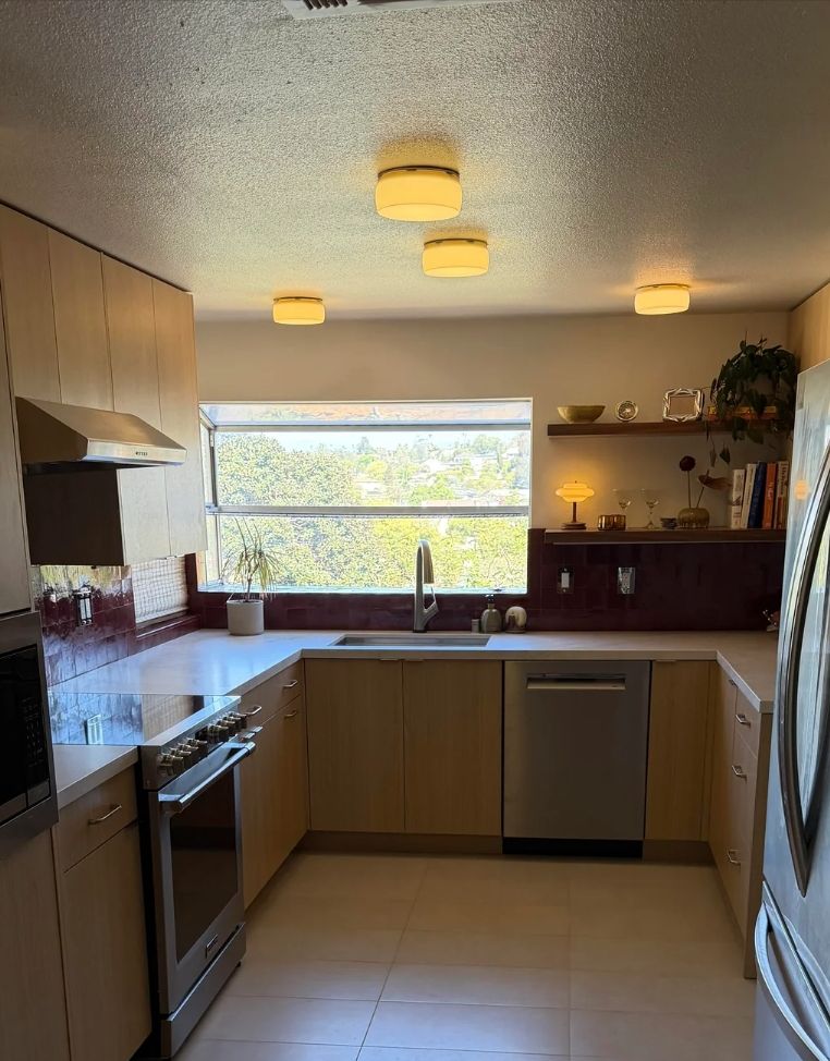 Finished small U-shaped kitchen: light wood cabinets, red tile backsplash, stainless appliances and a large window.