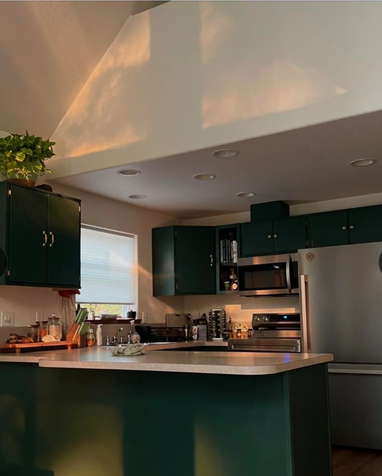 Kitchen after: cabinets and peninsula painted deep green with brass pulls and stainless appliances.